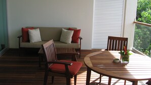 A wooden deck with a round table and two chairs, a sofa with patterned cushions, and a window with a view of greenery. - Vidanta Golf and Spa Resort 1 bedroom Grand Luxxe suite (Playa del Carmen)