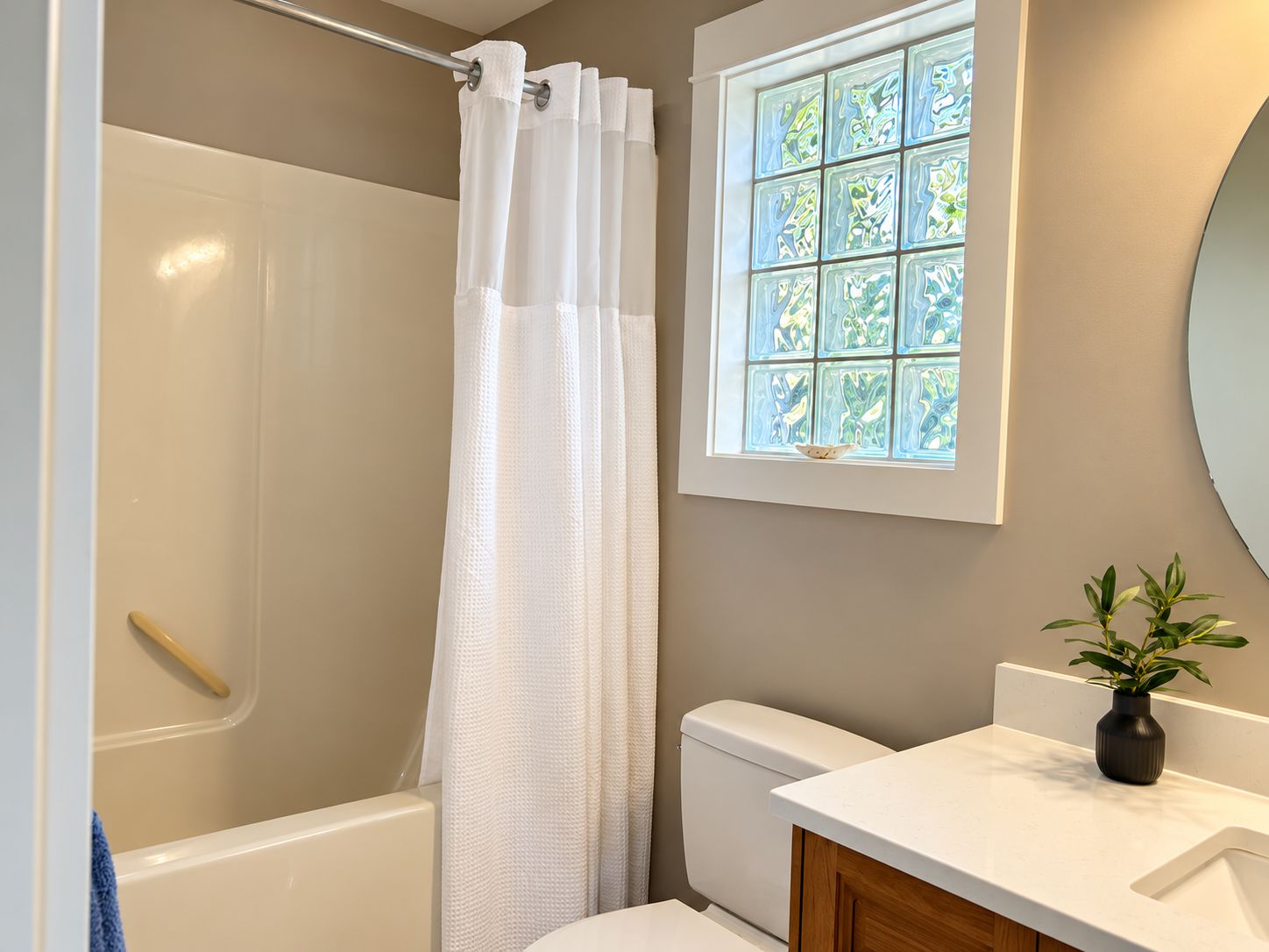A bathroom with a shower, toilet, sink, and a window with a view.