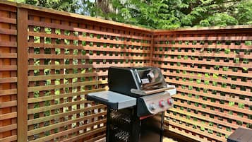 A portable barbecue grill with a digital display and control knobs, positioned on a wooden deck with a lattice fence in the background.