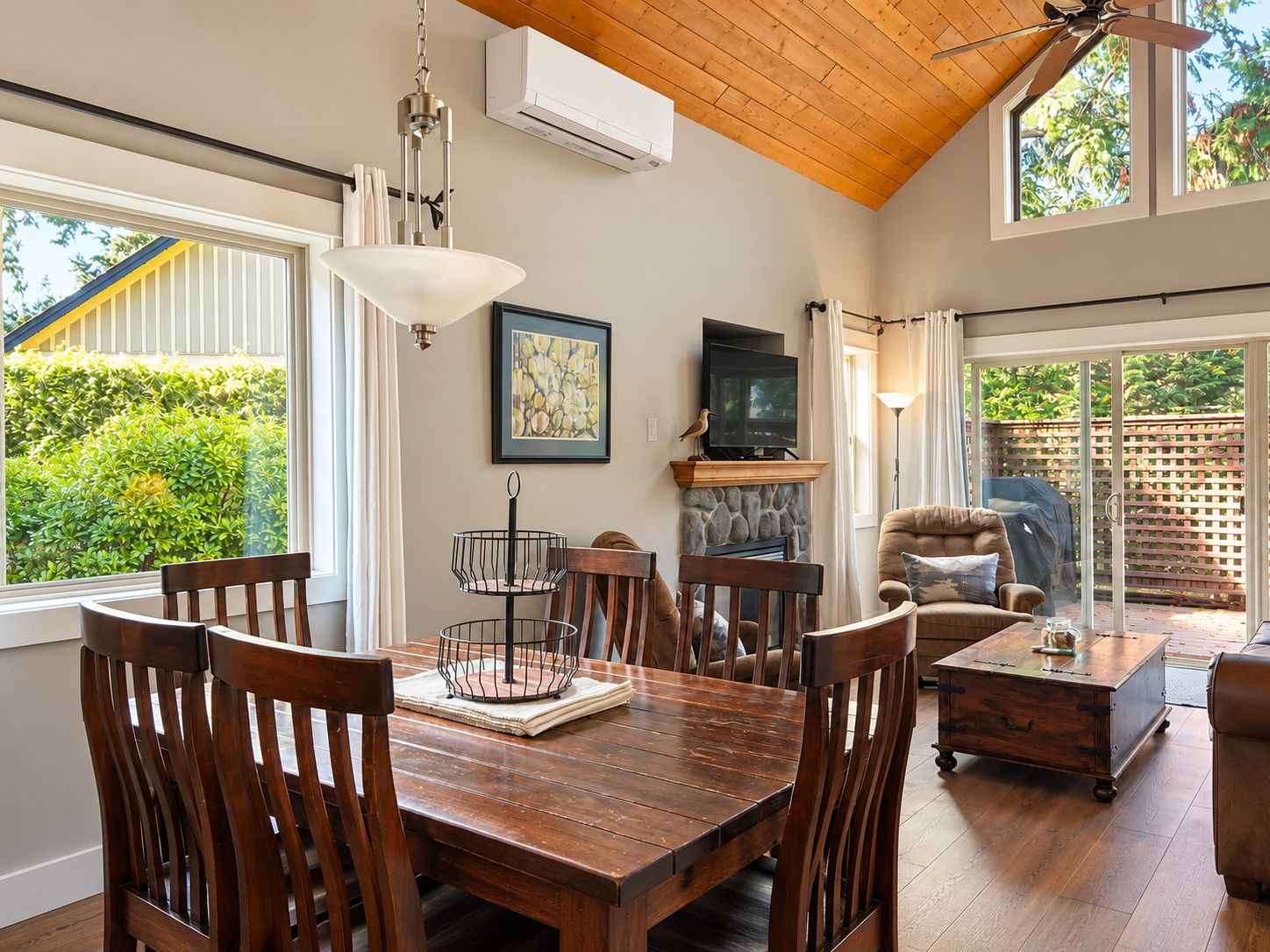 A dining area with a wooden table, chairs, a hanging light fixture, a fireplace, and a television.