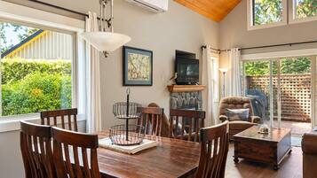 A dining area with a wooden table, chairs, a hanging light fixture, a fireplace, and a television.