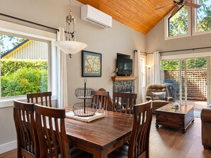 A dining area with a wooden table, chairs, a hanging light fixture, a fireplace, and a television.