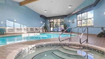 Una piscina interior con solárium de baldosas, una habitación luminosa con paredes azules y vistas al exterior a través de grandes ventanales.