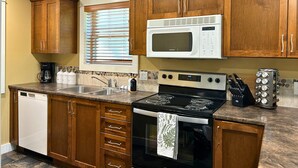 A kitchen with wooden cabinets, a microwave, a stove, a dishwasher, and a window with blinds.