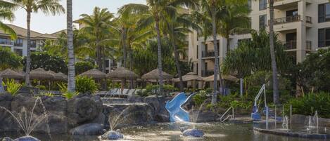 A resort pool area with palm trees, lounge chairs, and a water slide.