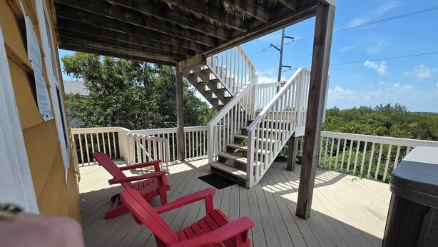 A wooden deck with a covered area, a staircase, and two red Adirondack chairs. - Ocean & sound views, hot tub, in Nags Head. (Nags Head)