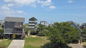 A coastal residential area with multiple two-story houses, a clear sky, and a grassy lawn. - Ocean & sound views, hot tub, in Nags Head. (Nags Head)
