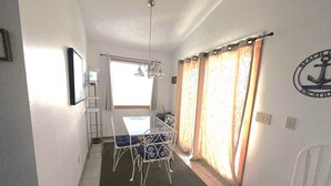 A dining area with a table and chairs, a window with curtains, and a wall with a logo. - Ocean & sound views, hot tub, in Nags Head. (Nags Head)