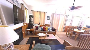 A living room with a sofa, a coffee table, a TV, and a dining area with a table and chairs. - Ocean & sound views, hot tub, in Nags Head. (Nags Head)
