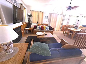 A living room with a sofa, a coffee table, a TV, and a dining area with a table and chairs. - Ocean & sound views, hot tub, in Nags Head. (Nags Head)