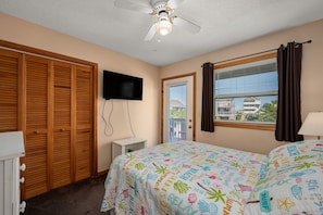 Quarto com cama, televisão, ventoinha no teto e janela com cortinas.