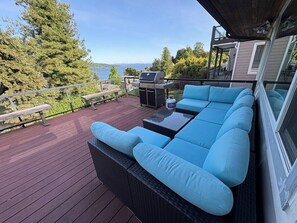 Une terrasse avec un canapé et un barbecue, donnant sur un plan d’eau.