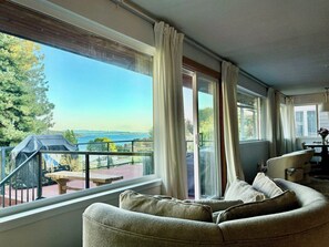 A living room with a sofa, a table, and a view of a balcony with a table and chairs. - Mt. Rainier & Lake Washington views - cozy 3BR guest suite in Lake Forest Park (Lake Forest Park)