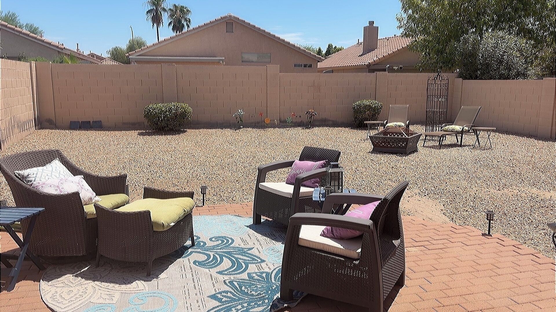 An outdoor patio area with wicker furniture, a fire pit, and a decorative rug.