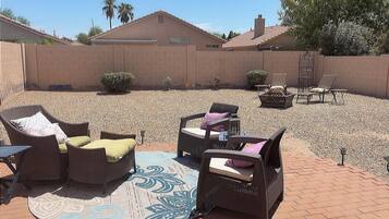 An outdoor patio area with wicker furniture, a fire pit, and a decorative rug.