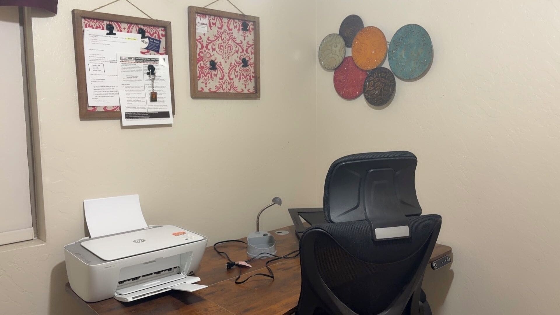 Une pièce équipée d’une imprimante, d’une chaise, d’un bureau et de deux panneaux d’affichage au mur.