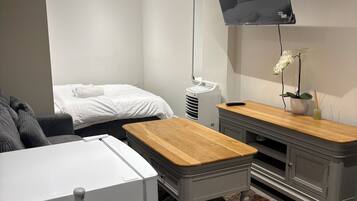 Quarto moderno com cama, frigorífico branco, mesa de madeira, armário cinzento e televisão na parede.