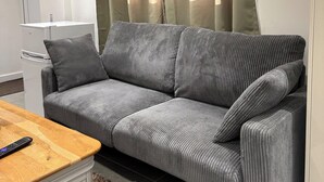 Un sofá gris con una mesa de centro de madera en una habitación con un armario blanco y una ventana con cortinas.