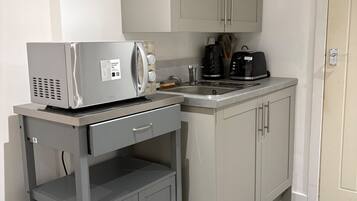 A kitchenette with a microwave, toaster, and coffee maker on a cart, a sink, and cabinets.
