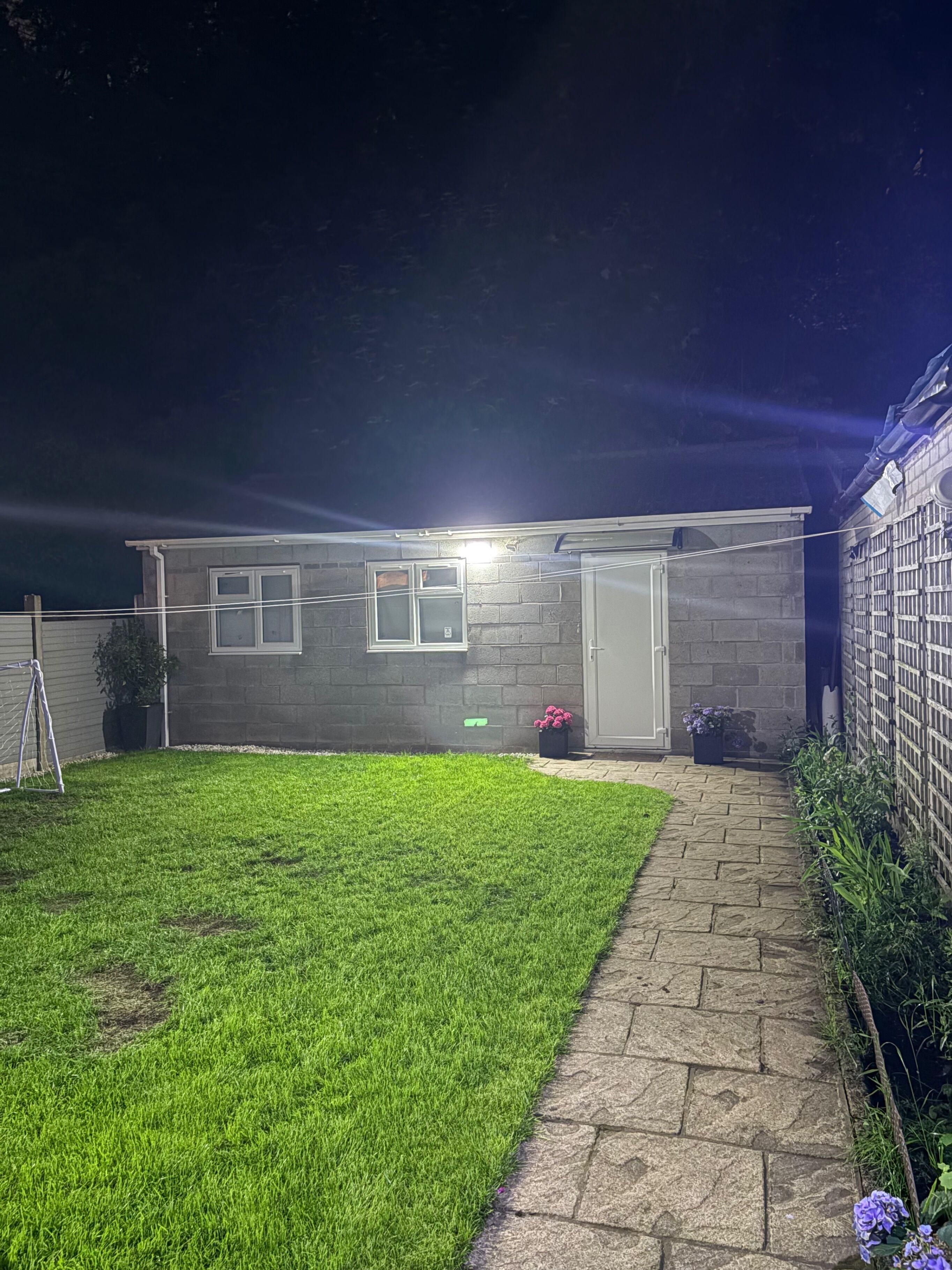 A residential property at night with a well-lit exterior, a paved driveway, and a grassy lawn.