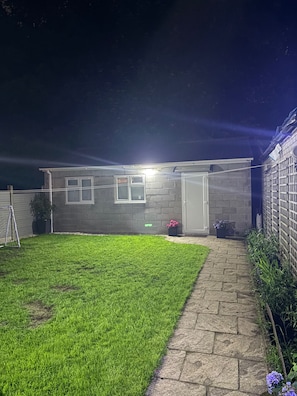 A residential property at night with a well-lit exterior, a paved driveway, and a grassy lawn. - Guesthouse Sleeps 2 with Parking (Bootle)