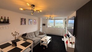A modern living room with a sofa, dining table, and a view of the outdoors. - Apartment Sleeps 2 with Free Parking (Orpington)