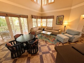 A sunlit living room with a checkered floor, a round table with chairs, a sofa, and a loveseat. - Orlando | Island Living Group Stay | Pool + Golf | 3BR Sleeps 12 (Lake Buena Vista)