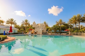 A swimming pool with a castle-like structure in the background, surrounded by palm trees and lounge chairs. - Orlando | Island Living Group Stay | Pool + Golf | 3BR Sleeps 12 (Lake Buena Vista)