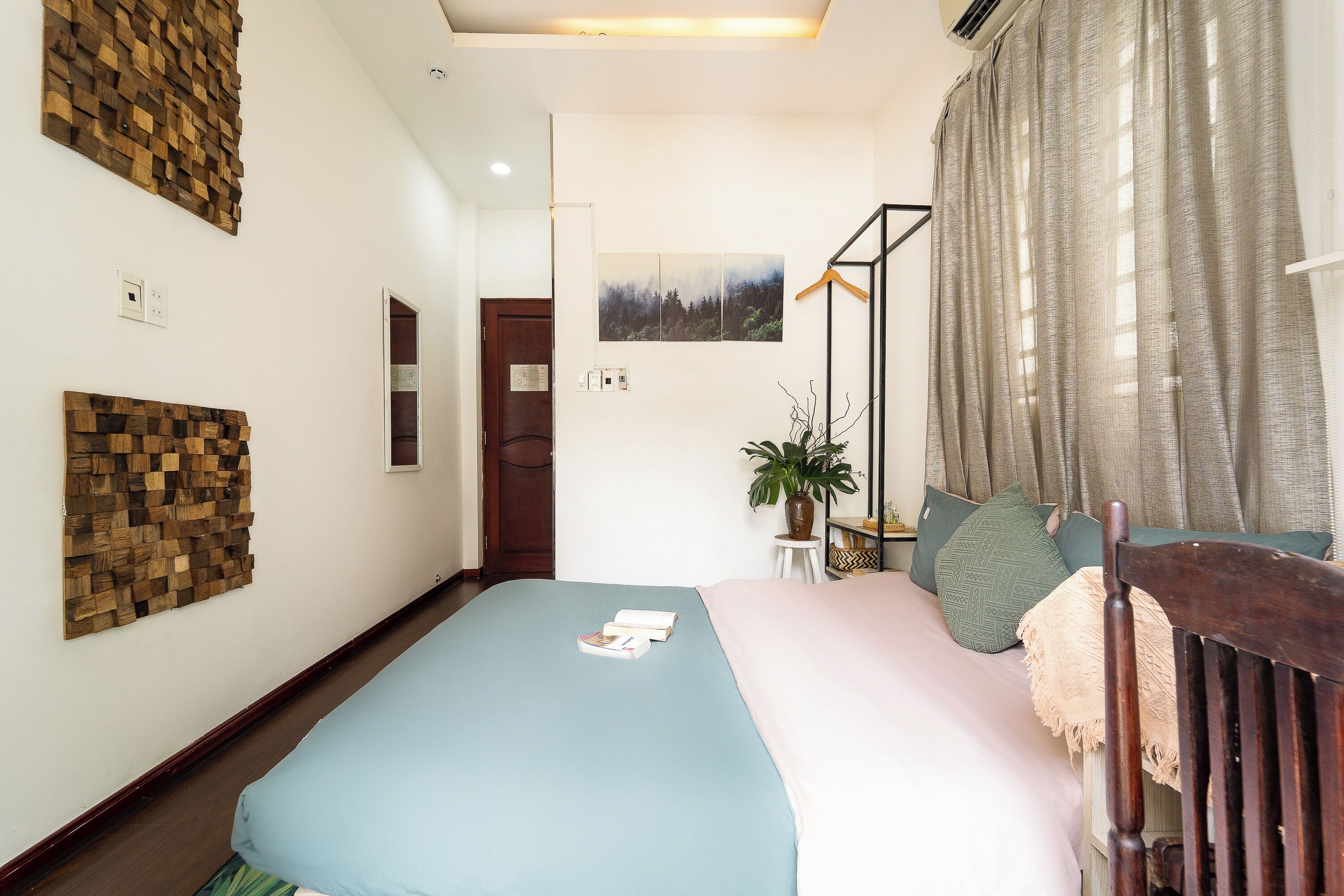 A bedroom with a bed, a wooden headboard, a wall-mounted shelf, a door, and a window with curtains.