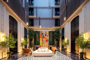 Un hall de hotel con una zona de estar central, una gran obra de arte colorida en la pared de fondo y plantas en macetas.