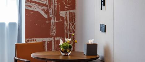 A round table with a vase of flowers, a tissue box, and a chair in a room with a patterned wall and a window.