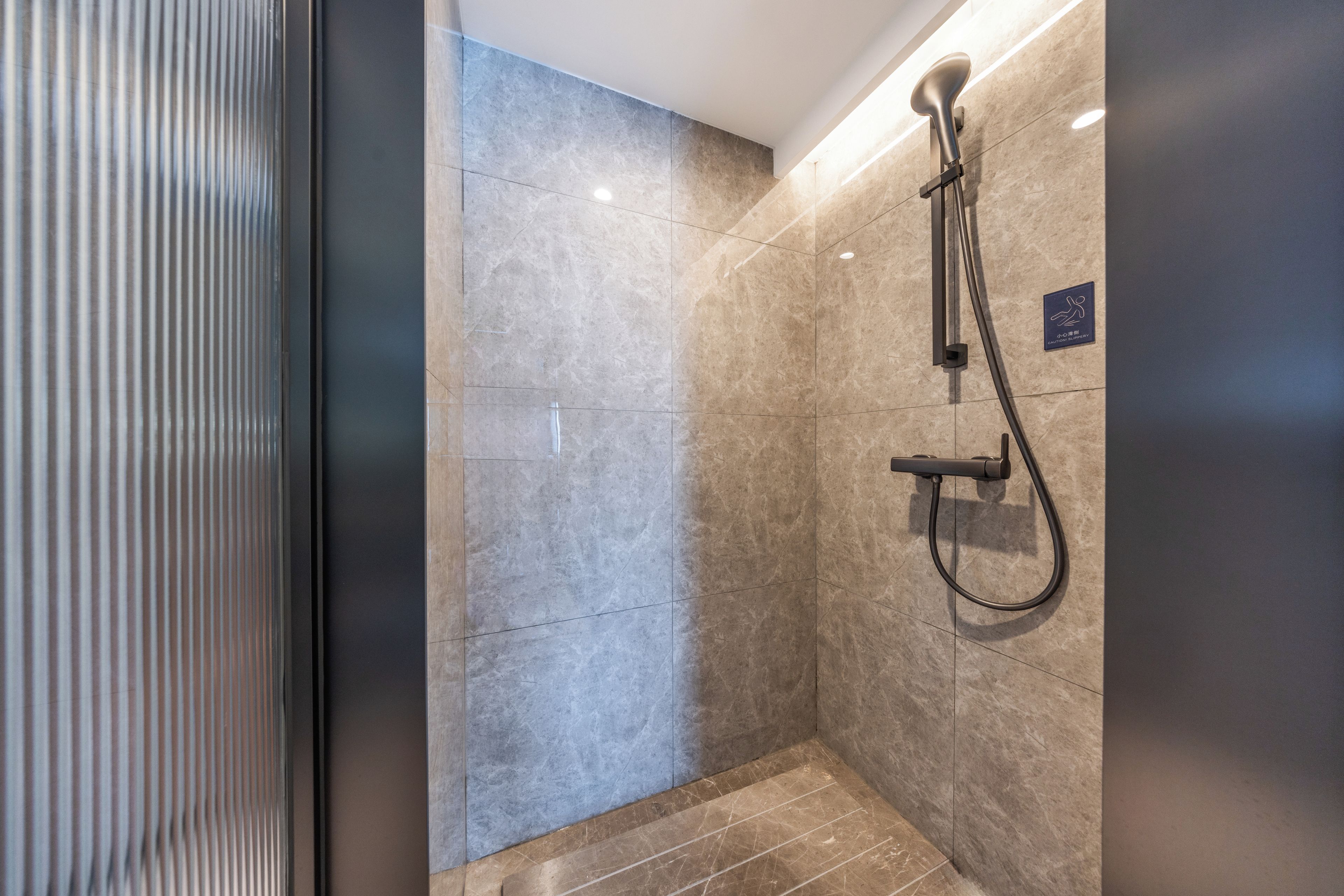 Un espacio de ducha moderno con cabezal de ducha de mano y panel de control en la pared.