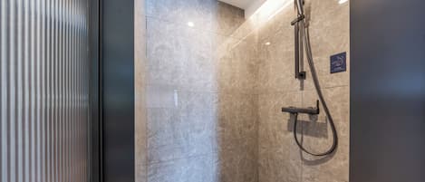 Uma área de chuveiro moderna com chuveiro manual e painel de controle fixado na parede.