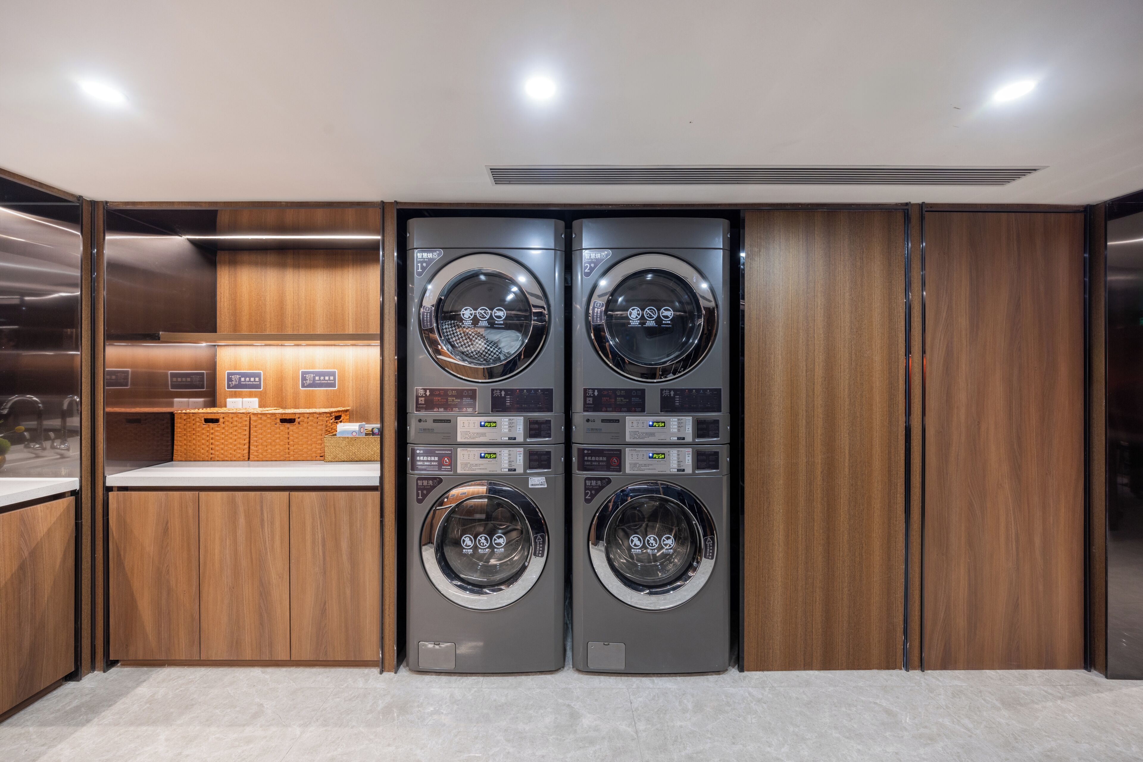 A laundry facility with two washing machines, wooden cabinets, and a counter with baskets.