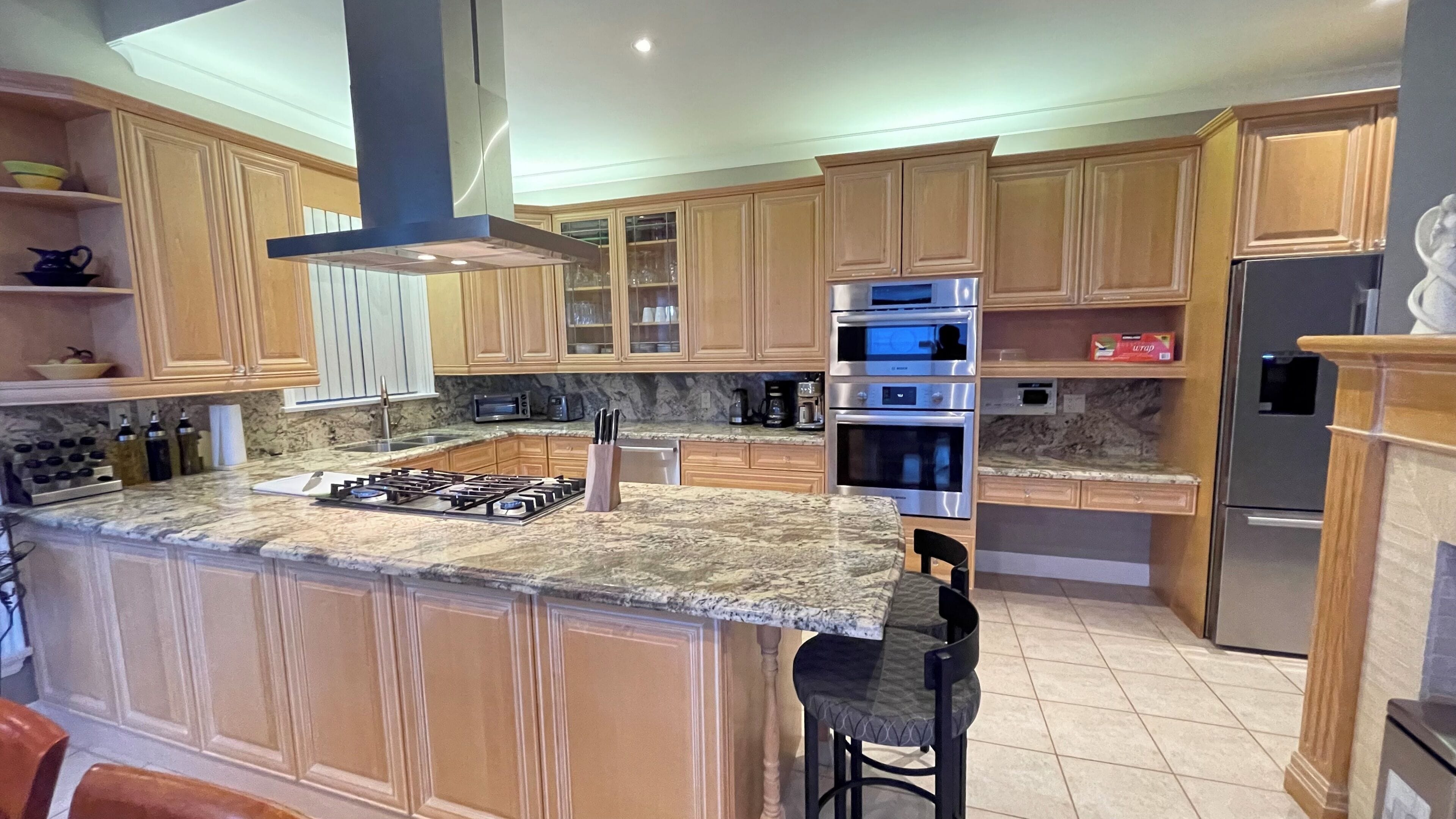 A kitchen with wooden cabinets, a gas stove, stainless steel appliances, and a marble countertop.