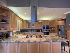 A modern kitchen with granite countertops, stainless steel appliances, wooden cabinets, and a central island.