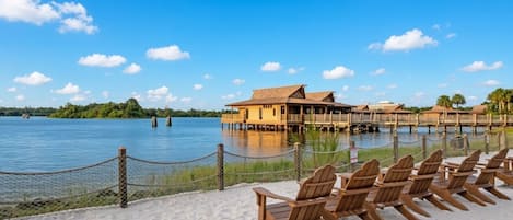 Un resort frente a la playa con cabañas de madera, una playa de arena y un lago tranquilo.