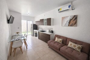 A modern kitchen with a dining area, a sofa, and a TV mounted on the wall.