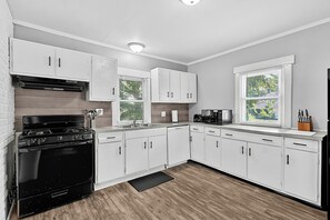 A modern kitchen with white cabinets, a black stove, and a window with blinds.