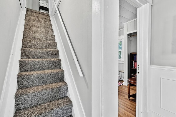 A staircase with carpeted steps leading to a room with a wooden floor, white walls, and a door.