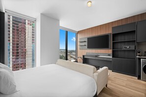 A modern hotel room with a large bed, a TV mounted on the wall, and a view of the cityscape through a large window. - Elegant E11EVEN Residence with ELITE Amenities (Miami)