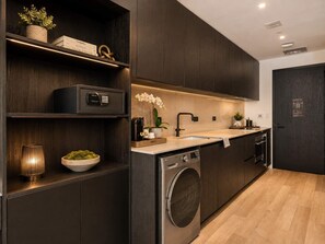 A modern kitchen with dark cabinetry, a built-in washing machine, and a countertop with a coffee machine. - Elegant E11EVEN Residence with ELITE Amenities (Miami)