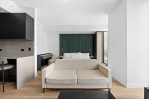 Ein modernes Hotelzimmer mit Schlafsofa, einer kleinen Küchenzeile und Blick durch ein großes Fenster.