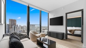 A modern living room with a large window, a sofa, a coffee table, and a TV mounted on the wall. - Luxury E11EVEN | Skyline Views & Resort Amenities (Miami)