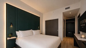 Een moderne hotelkamer met een groot bed, een nachtkastje met een plant, een donkere kast en een flatscreen televisie aan de muur.
