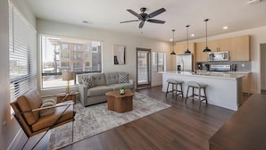 A modern living room with a sofa, coffee table, and a dining area with bar stools. - Landing | Modern 2BD, Game Room, Gym (Goodyear)