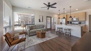 A modern living room with a sofa, coffee table, and a dining area with bar stools. - Landing | Modern 2BD, Game Room, Gym (Goodyear)