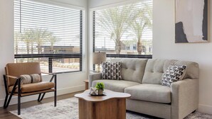 A living room with a sofa, armchair, coffee table, and a painting on the wall. - Landing | Modern 2BD, Game Room, Gym (Goodyear)