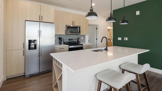 A modern kitchen with a large island, stainless steel appliances, and pendant lighting. - Landing | Modern 2BD, Game Room, Gym (Goodyear)