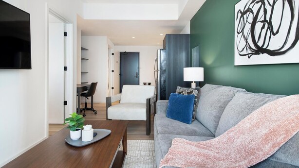 A modern living room with a grey sofa, a coffee table, a TV, and a painting on the wall. - Landing | Incredible 1BD, Courtyard (Orlando)